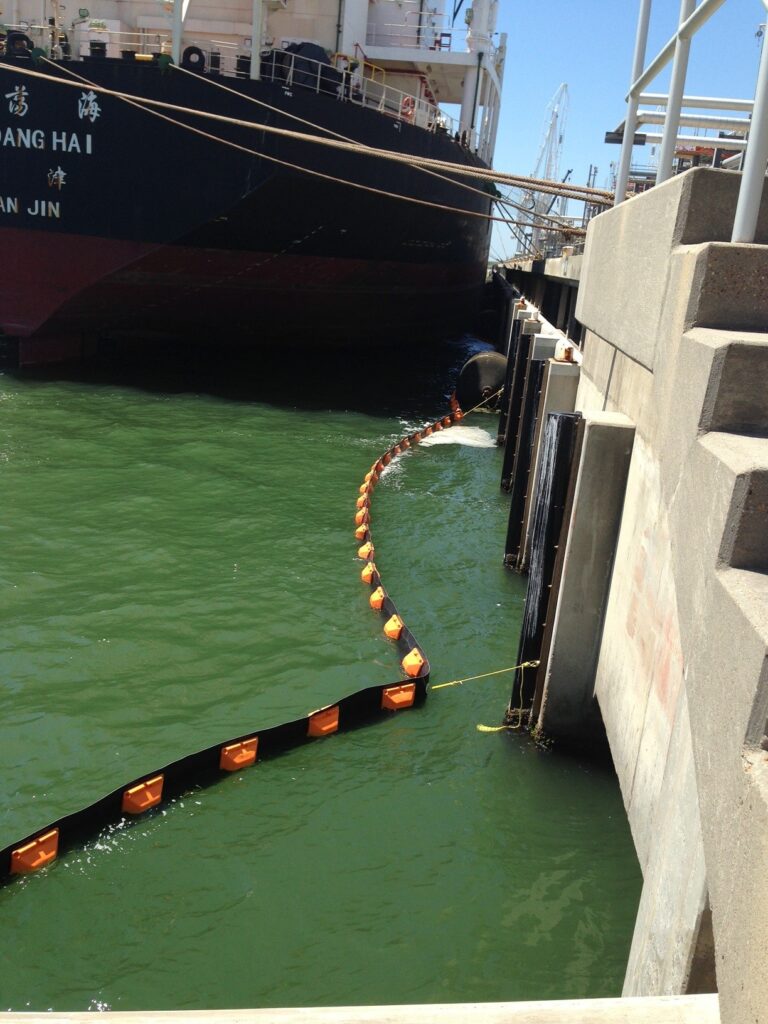 ACME Perma Boom deployed around a harbor pier while large ship docks