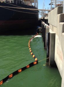 ACME Perma Boom deployed around a harbor pier while large ship docks